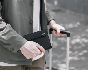DailyObjects Lounge Passport Wallet in black being held at an airport — slim travel document holder for passports, IDs, and cards.