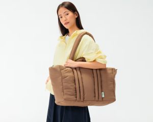 Woman carrying DailyObjects Puft Oversized Tote in brown — lightweight puffy travel tote for holiday getaways and overpackers.