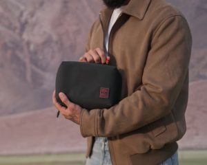 Man holding the Royal Enfield × DailyObjects Vault Tech Organiser — black travel pouch for tech accessories and grooming essentials.