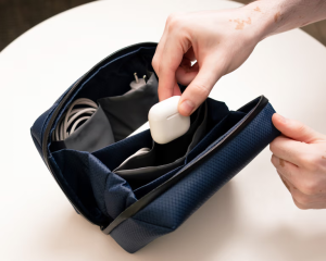 Hands placing AirPods inside a blue DailyObjects tech organiser — a practical Secret Santa gift for men who love tech.