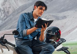 Rider sitting on a Royal Enfield motorcycle writing in the Royal Enfield x DailyObjects Field Notebook