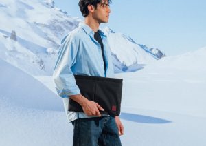 Rider holding the Royal Enfield x DailyObjects Laptop Sleeve while walking through a snowy mountain landscape